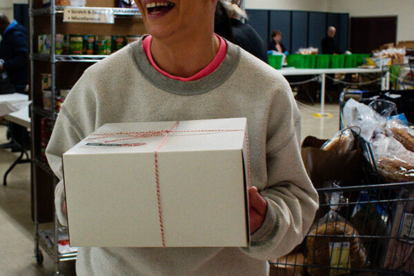 A woman holds a box of food at a food pantry in Warren, Rhode Island, and look away from the camera, laughing.