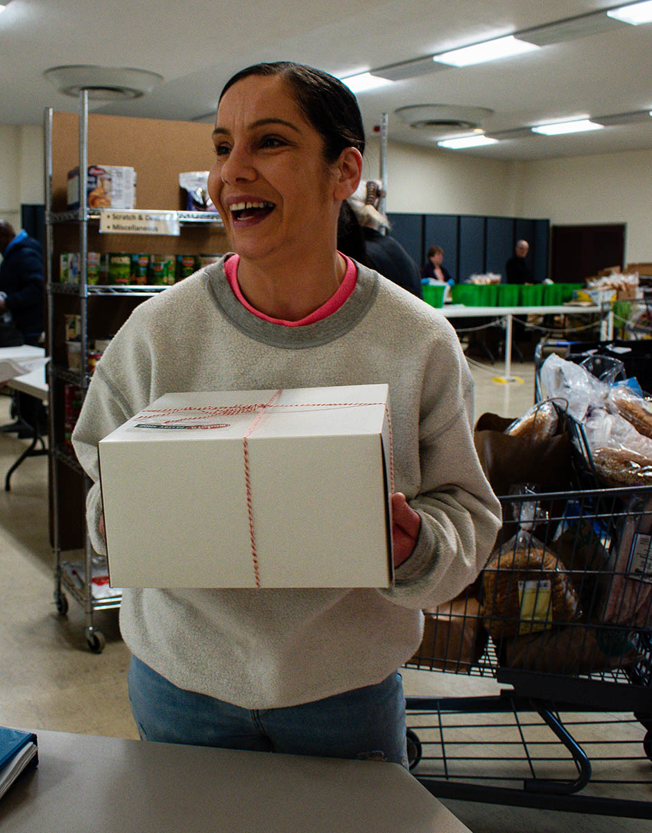 A woman holds a box of food at a food pantry in Warren, Rhode Island, and look away from the camera, laughing.