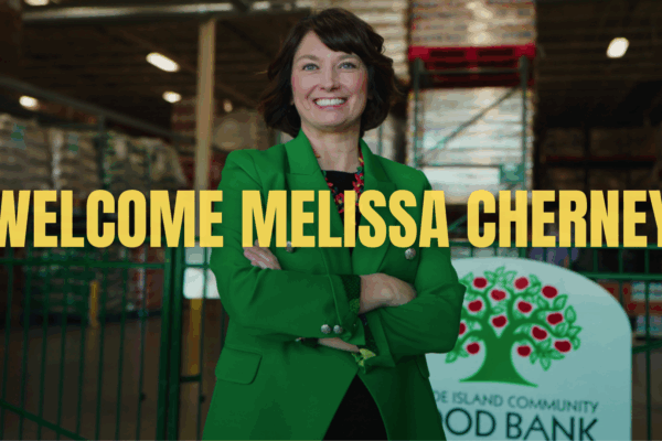 A woman, Melissa Cherney, CEO of the RI Community Food Bank, smiles with text that reads "Welcome Melissa Cherney"