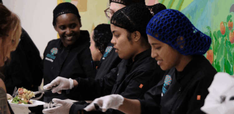 A group of people in Rhode Island Community Food Bank chef coats serve food to guests.