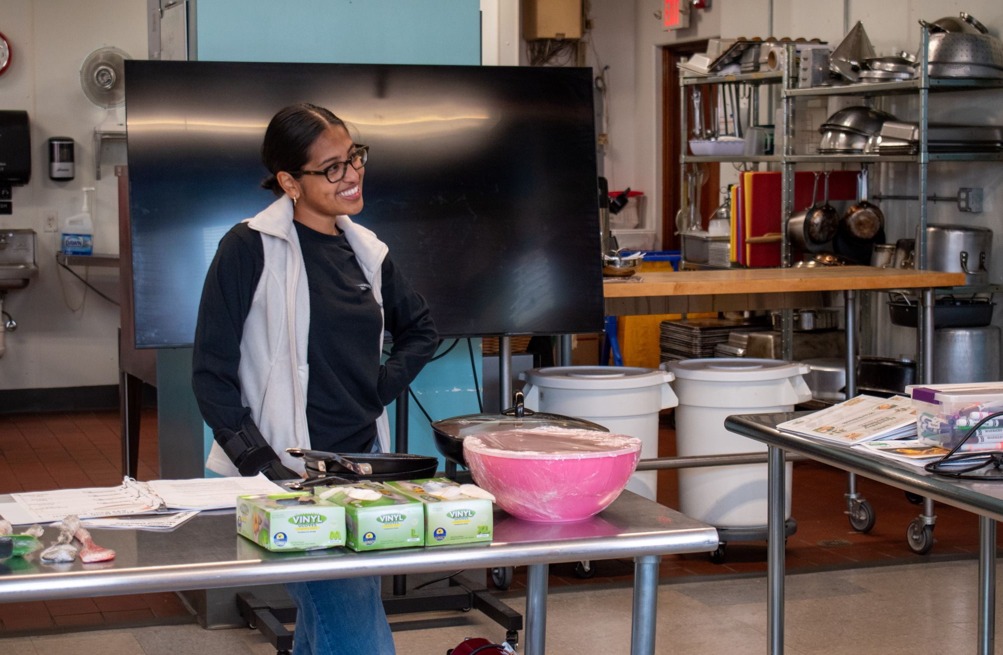 A woman Andrea Aguilar smiles while standing in front of ingredients and cooking supplies